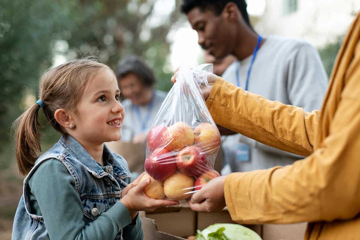 Child receiving a bag of fresh food from charity volunteers